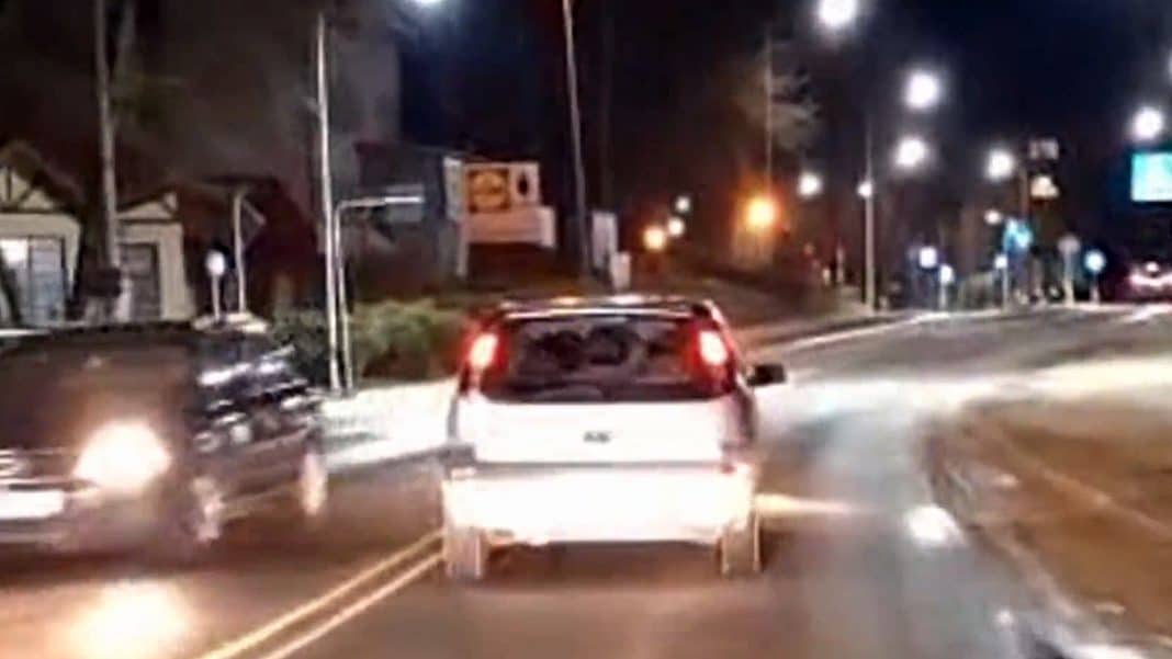 Zdjęcie przedstawia samoch&oacute;d na drodze w nocy, zbliżenie na tył pojazdu, w tle latarnie i inne auta.