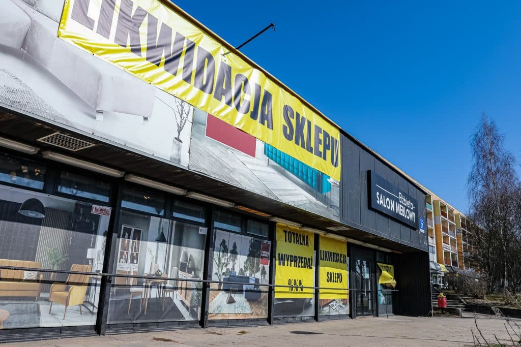 Widok z zewnątrz sklepu meblowego z dużym banerem wyprzedaży na fasadzie.
