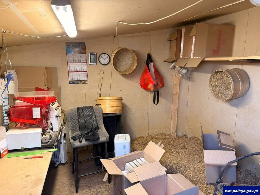 Wewnątrz pomieszczenia z urządzeniami i opakowaniami do produkcji papieros&oacute;w, na ścianach kalendarze i zegar.