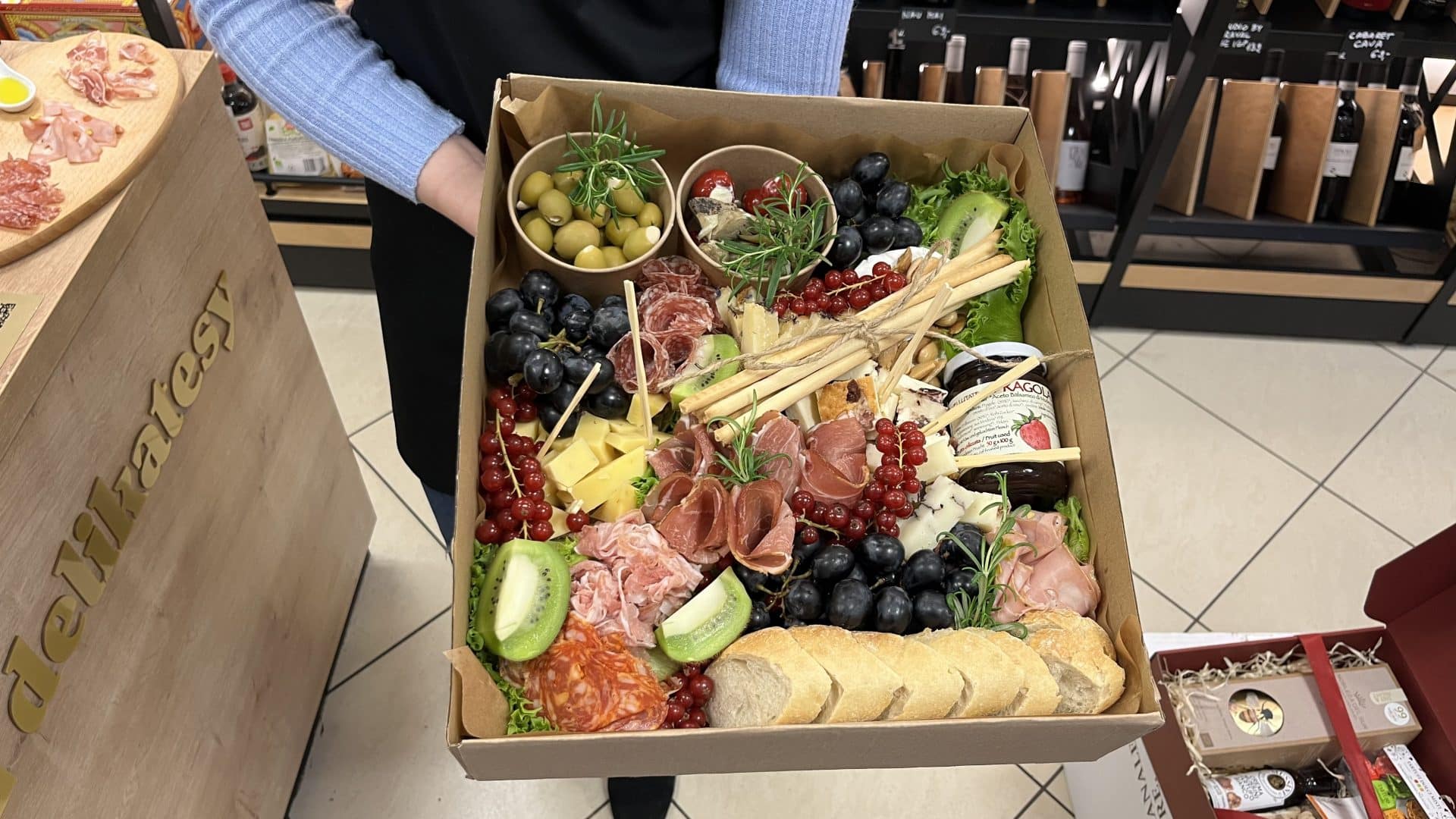 Duży box z r&oacute;żnorodnymi zdrowymi przekąskami, w tym wędlinami, serami, owocami i warzywami.