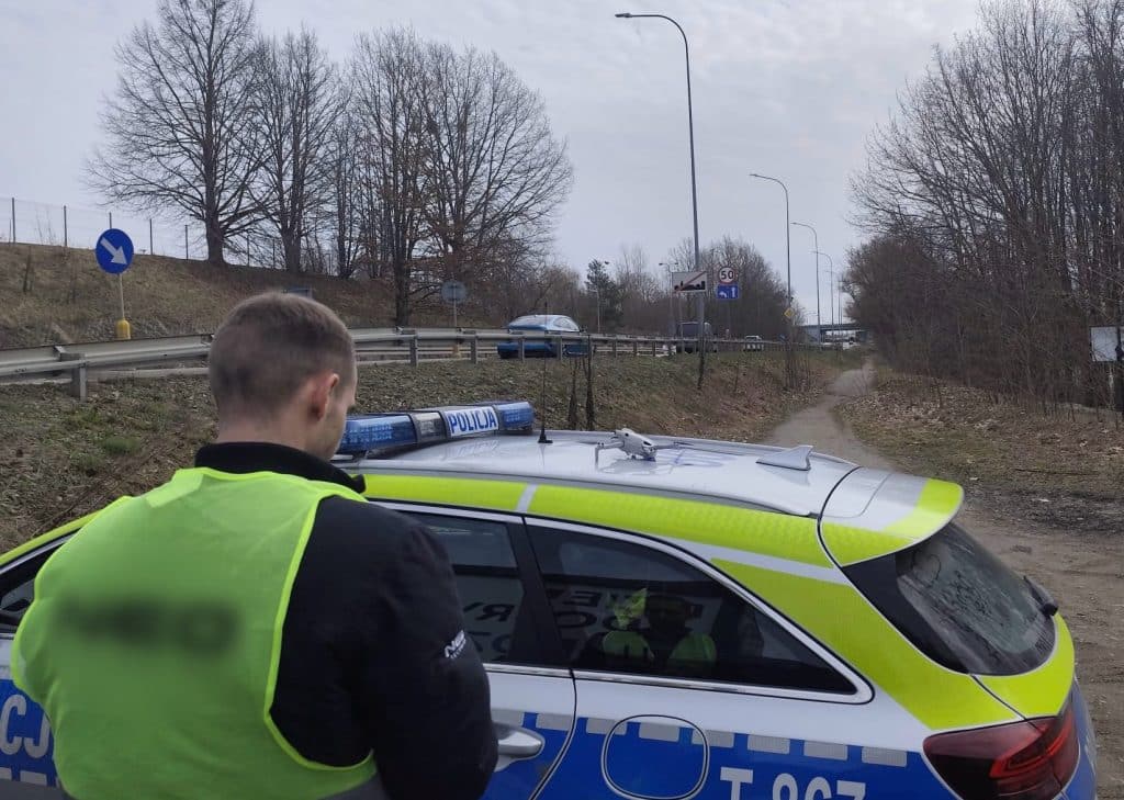 Policjant przy radiowozie podczas akcji poszukiwawczej nad jeziorem Sajmino.