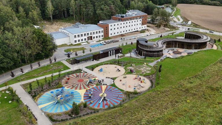 Widok na uzdrowisko w Lidzbarku Warmińskim z placem zabaw i budynkami w otoczeniu lasu i p&oacute;l.