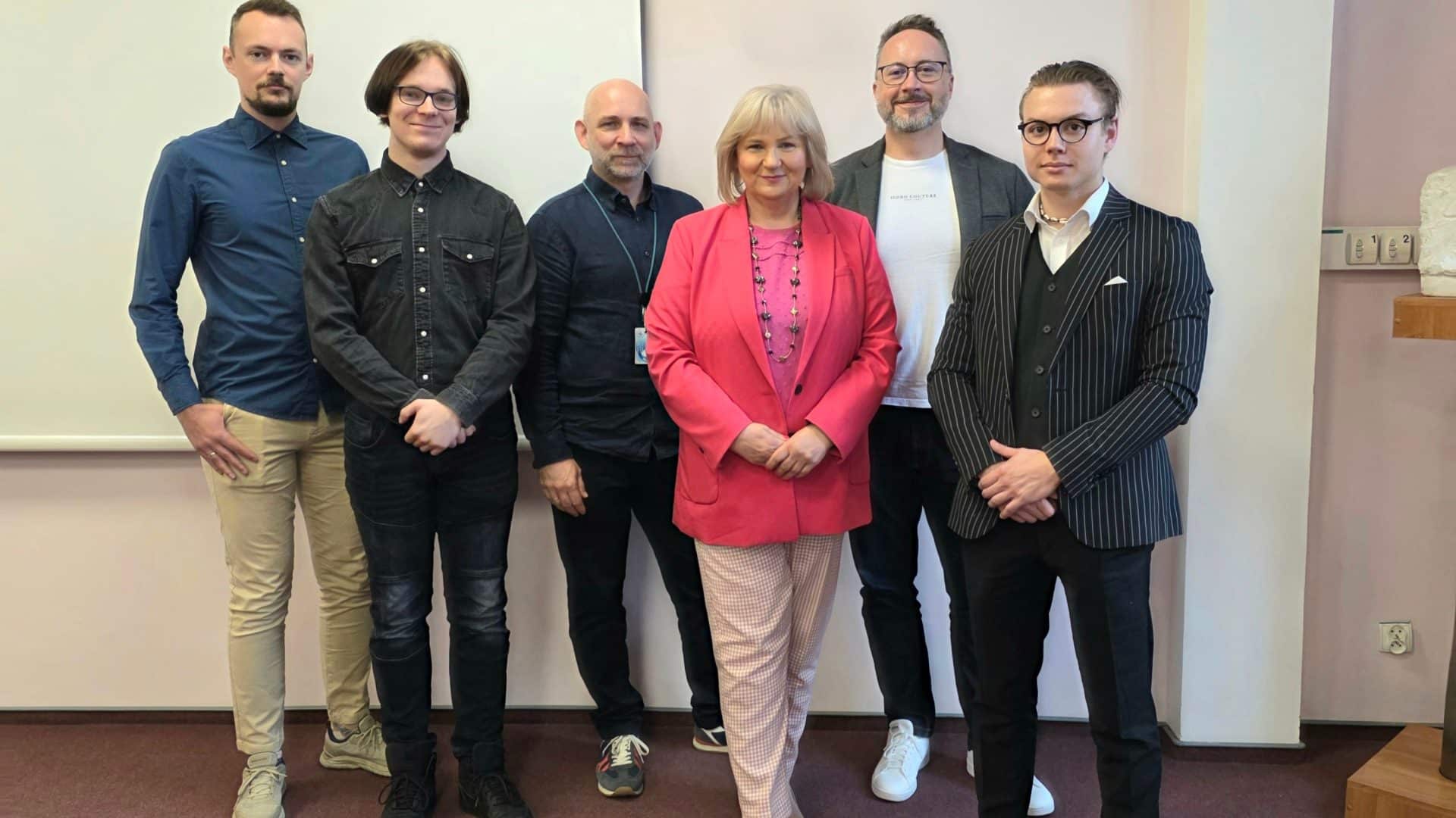 Grupa ludzi stojąca w pomieszczeniu, w tle białe ściany i elementy wyposażenia.