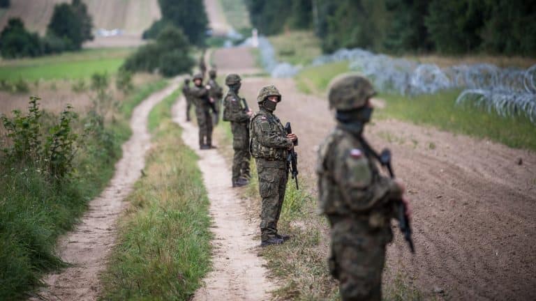 Grupa żołnierzy patrolujących granicę polsko-białoruską w terenie z drutem kolczastym w tle.
