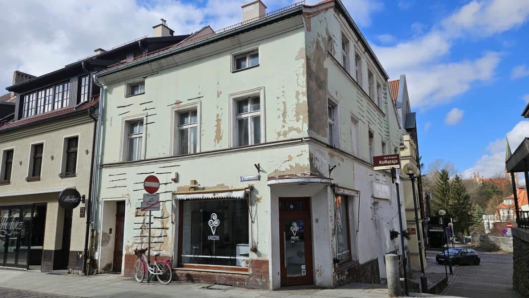 Stara, odrapana kamienica na ulicy w Olsztynie, z widocznymi śladami remontu i zniszczeń na elewacji.