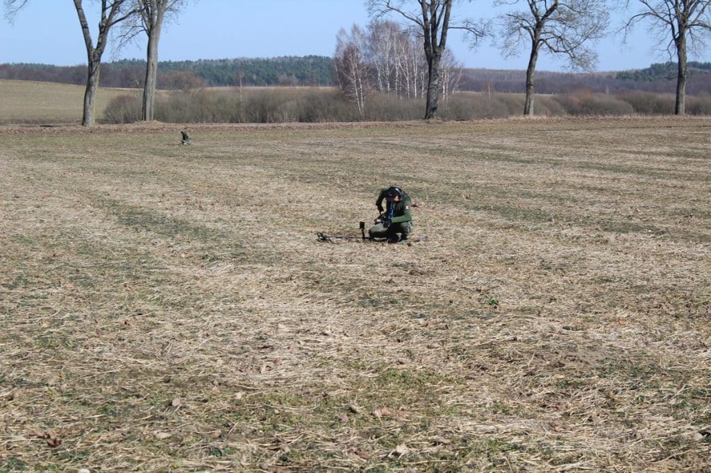Archeolog prowadzi wykopaliska na polu w okolicach wsi Leszcz, w tle drzewa i horyzont.