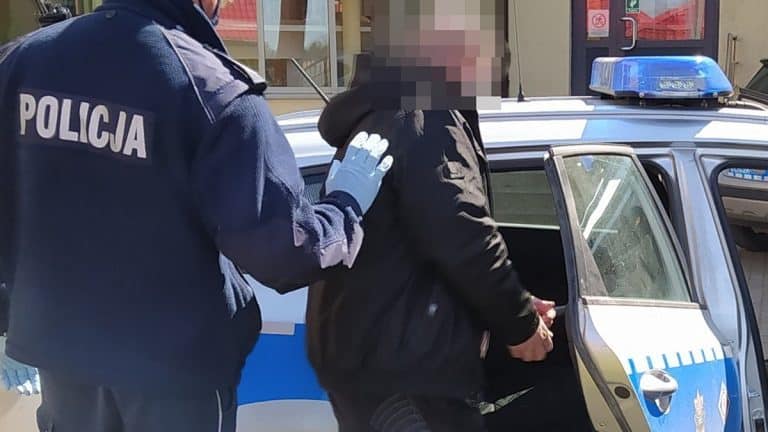 Policjant zatrzymuje mężczyznę przy radiowozie w miejscowości pod Olsztynem.