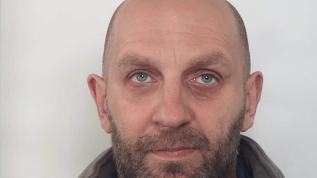 Zdjęcie mężczyzny z kr&oacute;tkim zarostem i blizną na czole, patrzącego w kamerę.