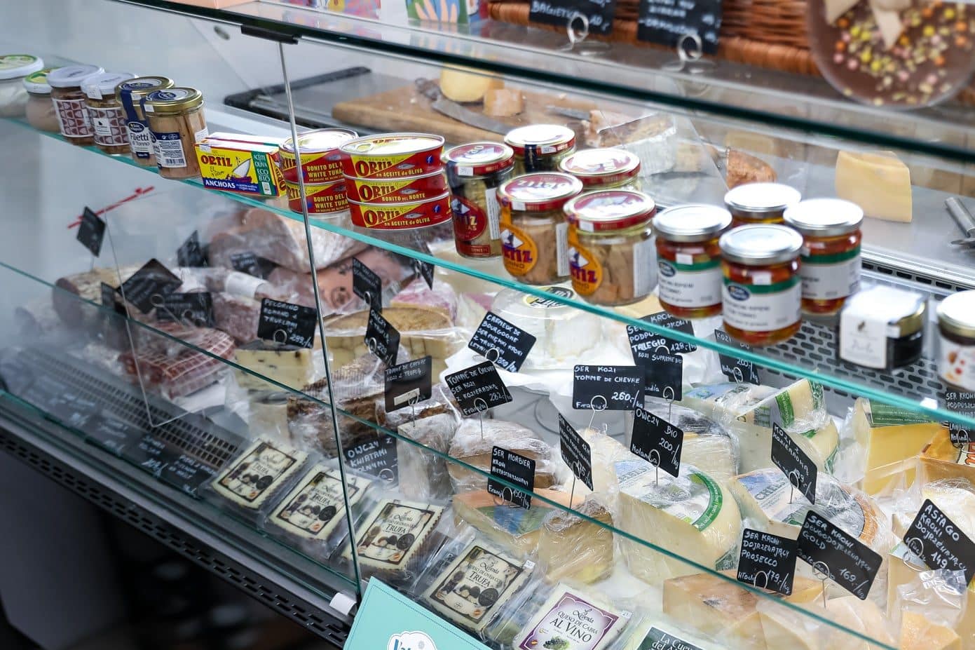 Wyświetlacz ser&oacute;w, wędlin i przetwor&oacute;w w sklepie spożywczym, na tle etykiet i cen.