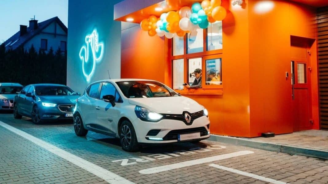 Samochody zaparkowane przed kolorowym budynkiem z neonowym logo w tle.