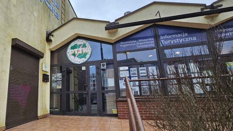 Budynek z logo regionalnej organizacji turystycznej na Warmii i Mazurach, widoczny napis 'Informacja Turystyczna'.