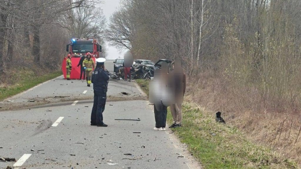 Wypadek drogowy z udziałem samochodu i służb ratunkowych na drodze w lesie.