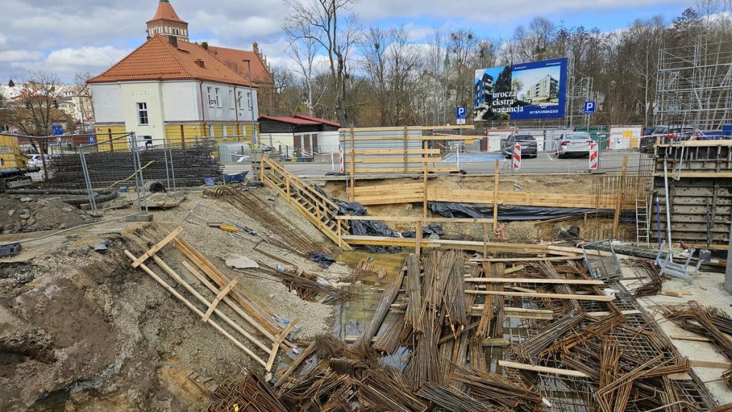 Trwa budowa nowego obiektu usługowego w centrum Olsztyna, widoczne wykopy i prace konstrukcyjne.