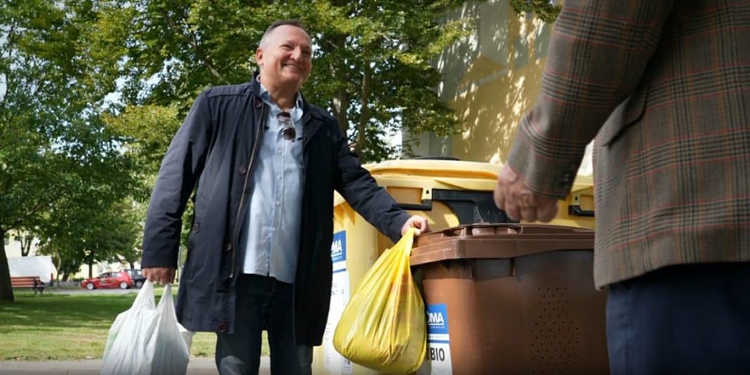 Mężczyzna wrzuca bioodpady do pojemnika na tle zielonego parku, uśmiecha się podczas segregacji odpad&oacute;w.
