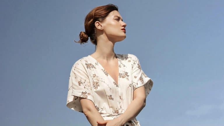 Kobieta w lekkiej, kwiatowej sukience na tle nieba, patrzy w bok, wyraz skupienia.