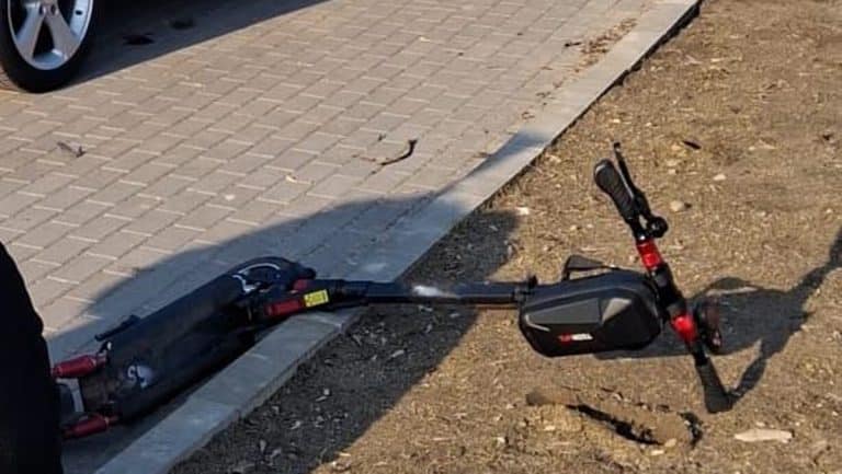 Złamana hulajnoga elektryczna na poboczu po kolizji na ścieżce rowerowej.