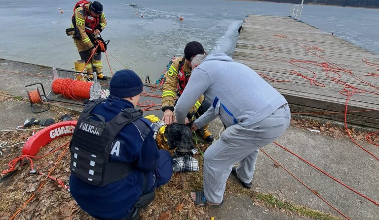 Strażacy i policja ratują psa z lodu na jeziorze, akcja ratunkowa na tle zamarzniętego jeziora.