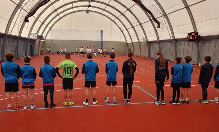 Dzieci i młodzież na nowym zadaszonym boisku sportowym w Dywitach, wewnątrz hali z łukowatym dachem.