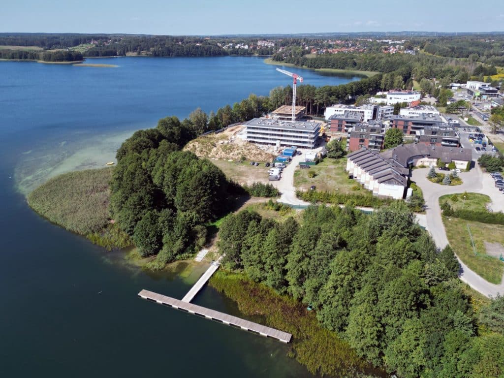 Widok na jezioro Ukiel w Olsztynie z nowo budowanymi obiektami i otaczającą zielenią.