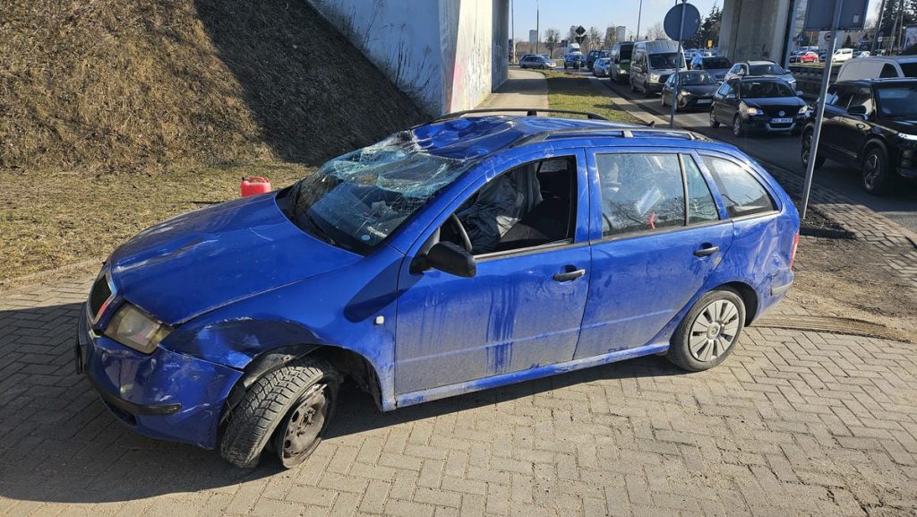 Uszkodzony niebieski samoch&oacute;d po dachowaniu na rondzie w Olsztynie, uszkodzone przednie koło i rozbite szyby.