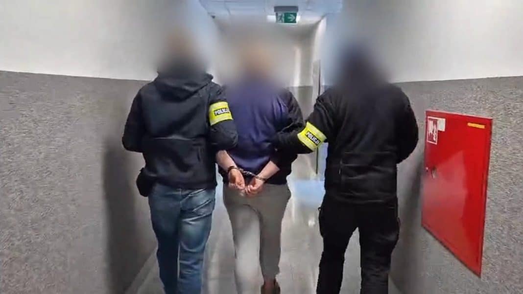 Mężczyzna w rękach policji prowadzony korytarzem, jego twarz jest zamazana.