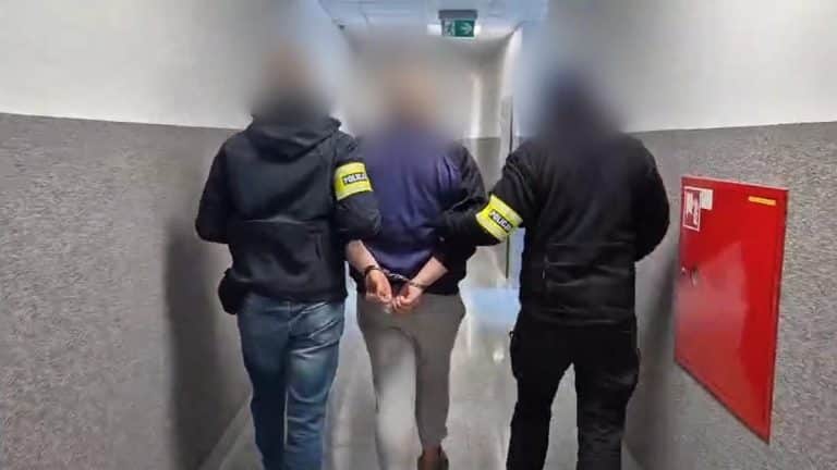 Mężczyzna w rękach policji prowadzony korytarzem, jego twarz jest zamazana.