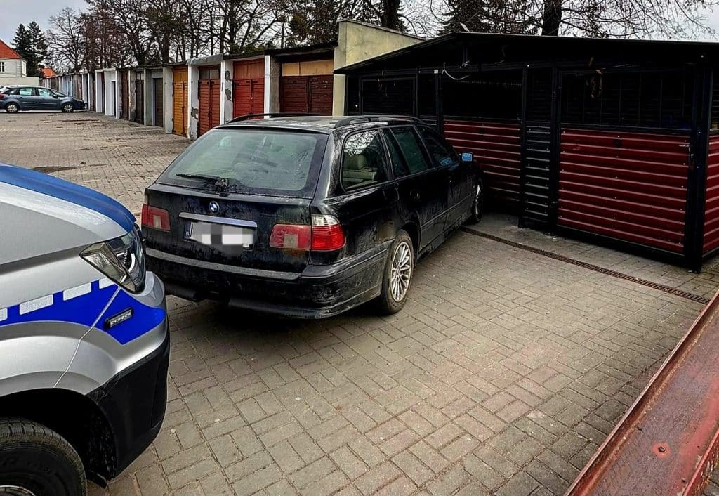 Czarny samoch&oacute;d marki BMW zaparkowany na osiedlu, obok policyjnego radiowozu.