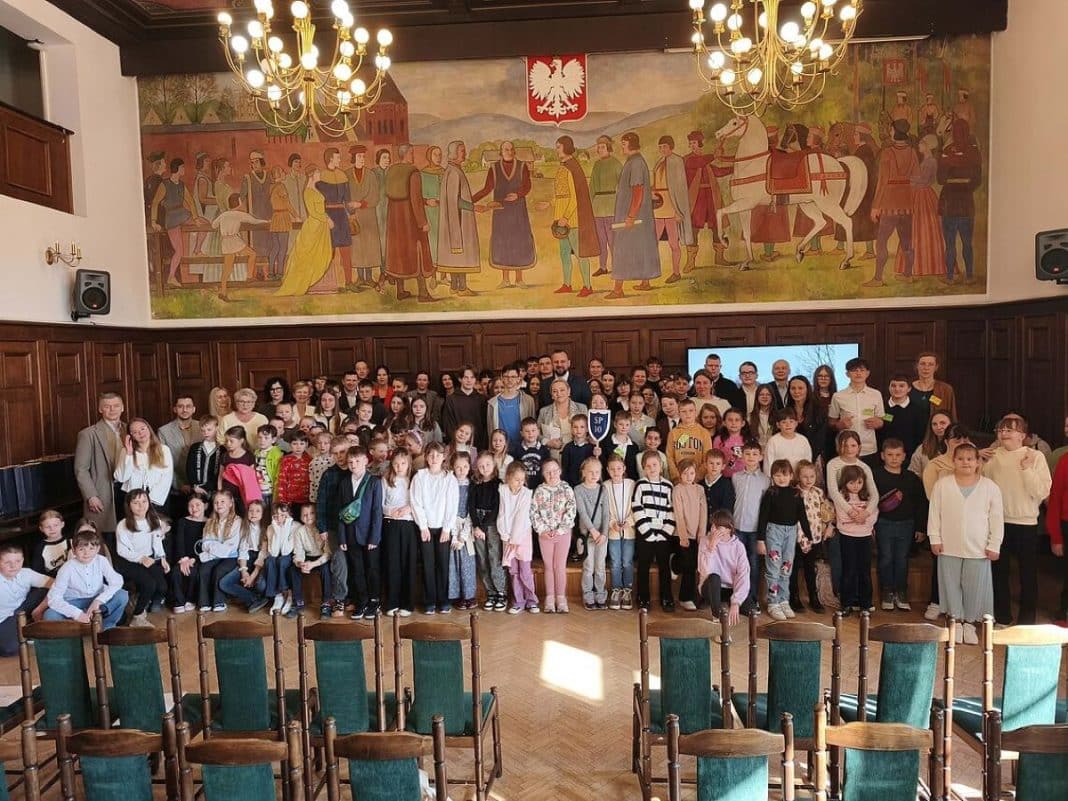 Grupa uczni&oacute;w i mieszkańc&oacute;w na oficjalnym podsumowaniu akcji sprzątania Olsztyna w ratuszu.