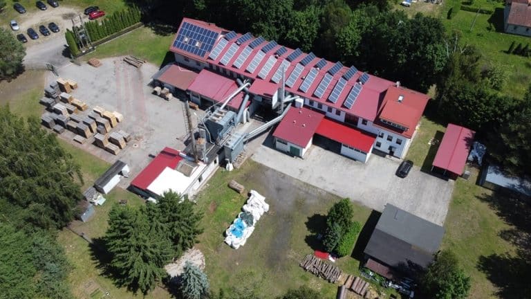 Widok z powietrza na zakład produkcyjny z czerwonymi dachami i otaczającą zieleń.