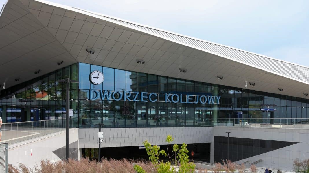 Widok nowoczesnego dworca kolejowego z dużym zegarem i nazwą w centrum.