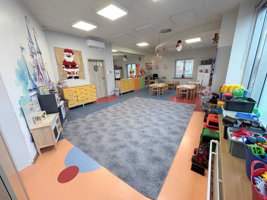 Wnętrze żłobka z kolorowymi zabawkami, dekoracjami świątecznymi i przestrzenią do zabawy.