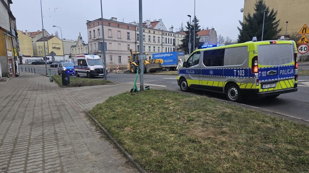 Zabezpieczone miejsce interwencji policji na osiedlu Grunwaldzkim w Olsztynie, widoczne radiowozy i sprzęt budowlany w tle.