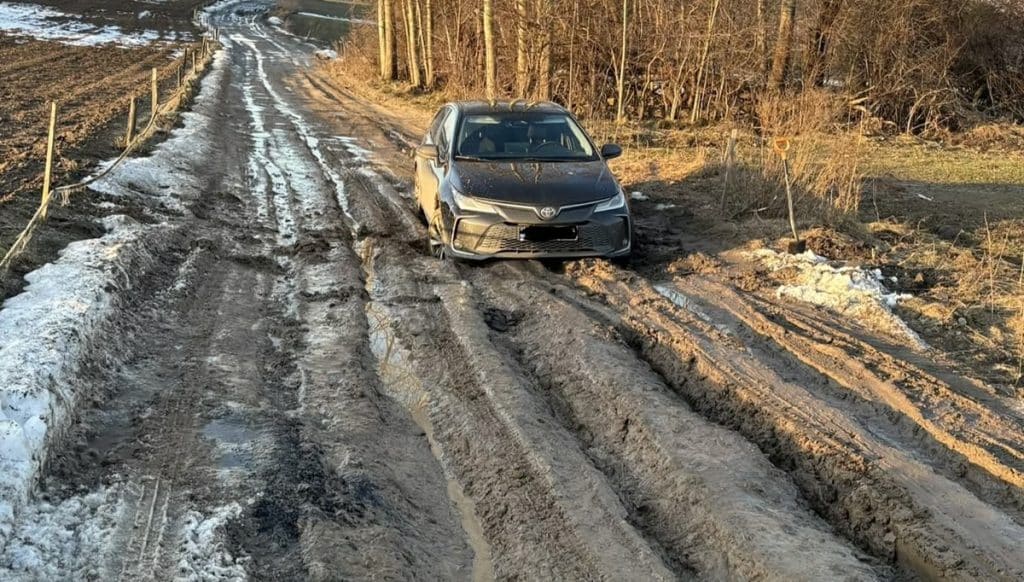 Zniszczona, błotnista droga w Redykajnach z samochodem na poboczu.