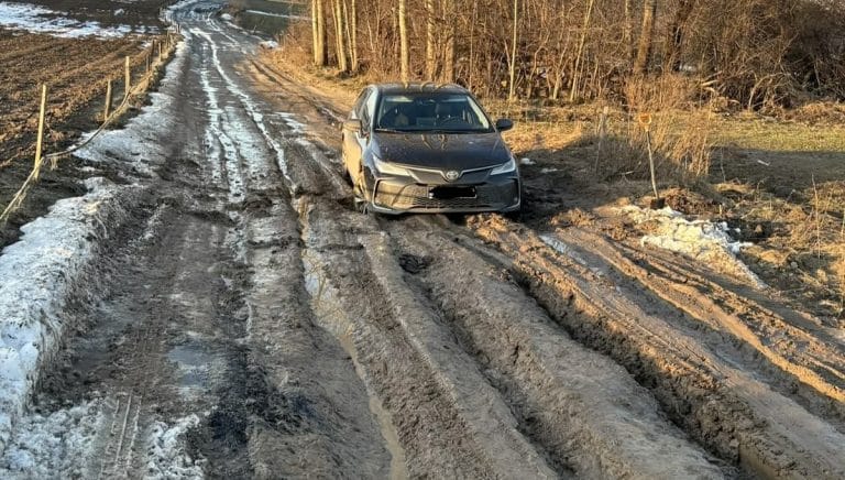 Zniszczona, błotnista droga w Redykajnach z samochodem na poboczu.