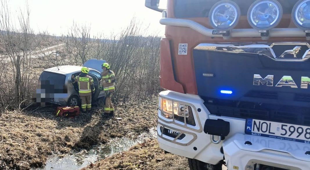 Strażacy udzielają pomocy po zderzeniu dw&oacute;ch samochod&oacute;w na drodze wojew&oacute;dzkiej, widok na pojazdy i służby ratunkowe.
