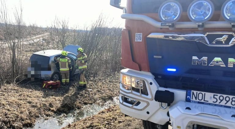 Strażacy udzielają pomocy po zderzeniu dw&oacute;ch samochod&oacute;w na drodze wojew&oacute;dzkiej, widok na pojazdy i służby ratunkowe.