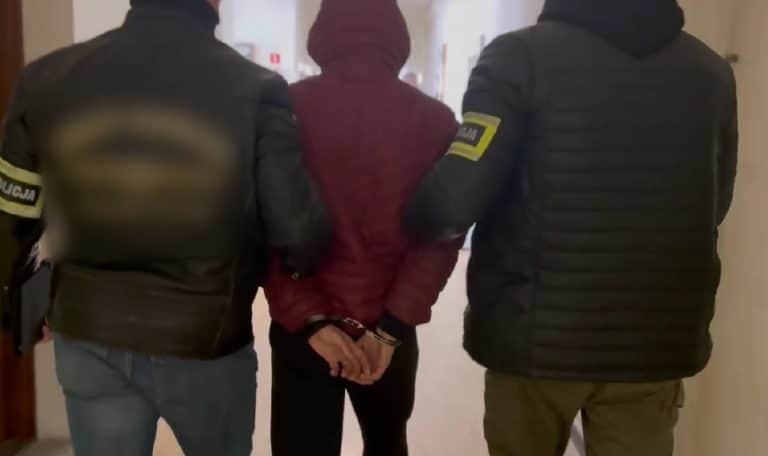 Mężczyzna w rękach policjant&oacute;w, odwr&oacute;cony plecami, w centrum zdjęcia, w pomieszczeniu.