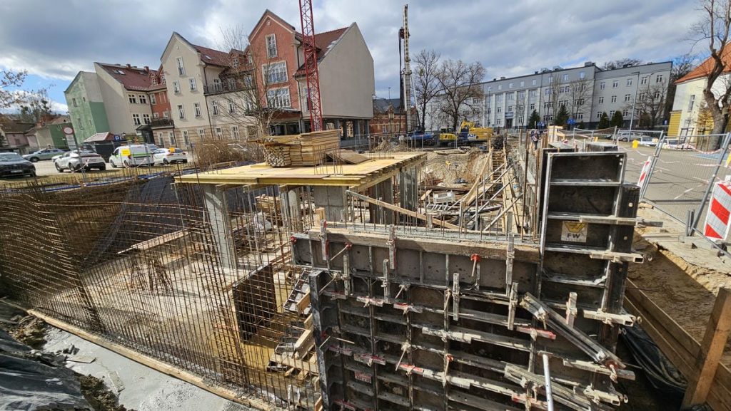Budowa nowego obiektu usługowego w centrum Olsztyna, widoczne prace ziemne i elementy konstrukcyjne.