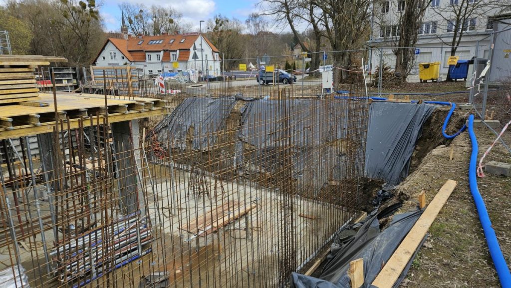Trwa budowa nowego obiektu hotelowo-gastronomicznego w centrum Olsztyna, widoczne prace ziemne i zbrojenia.