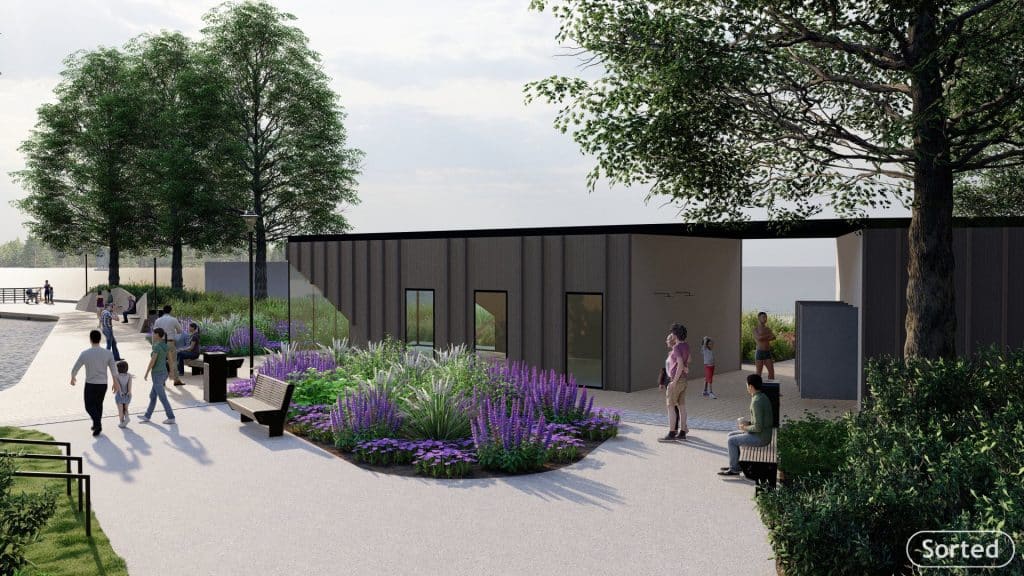 Nowoczesny obiekt rekreacyjny na plaży z zielenią i ławkami, w tle drzewa i nad wodą.