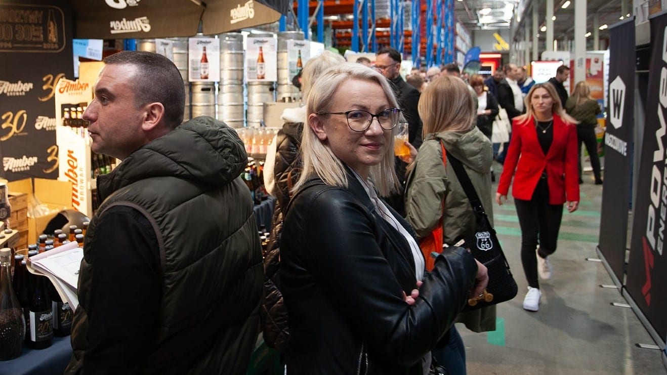 Tłum uczestnik&oacute;w na targach biznesowych w hali, stoiska z produktami i rozmowy biznesowe.