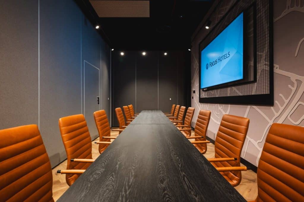 Nowoczesna sala konferencyjna z dużym ekranem i brązowymi krzesłami.