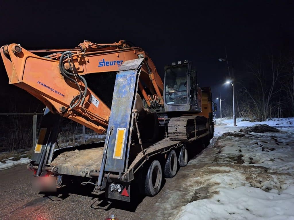 Ciężki pojazd na lawecie nocą na ulicy, oświetlony latarniami, z śniegiem na poboczu.