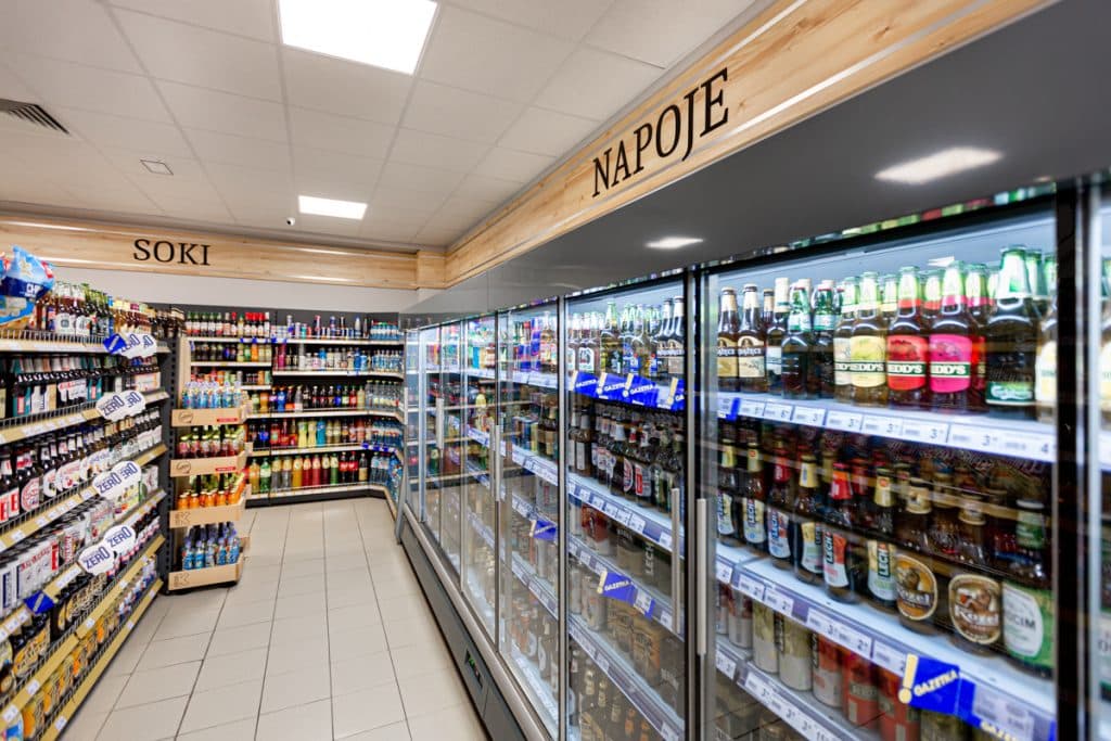 Wnętrze sklepu spożywczego z chłodziarkami i p&oacute;łkami z napojami i sokami.