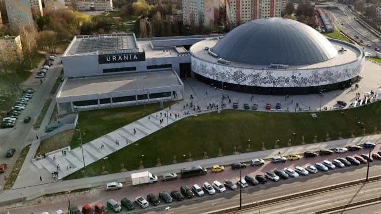 Widok na Halę Urania w Olsztynie z lotu ptaka, otoczona parkingami i zielenią.