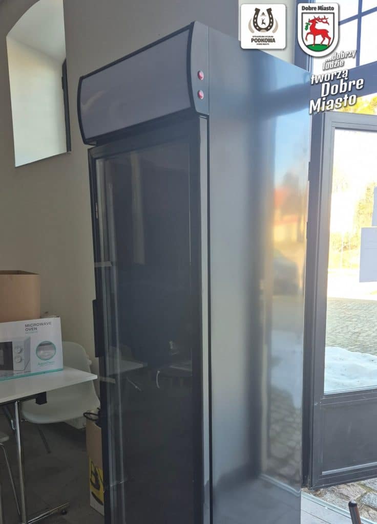Lod&oacute;wka społeczna ustawiona w pomieszczeniu przy wejściu do budynku, obok drzwi wejściowych.