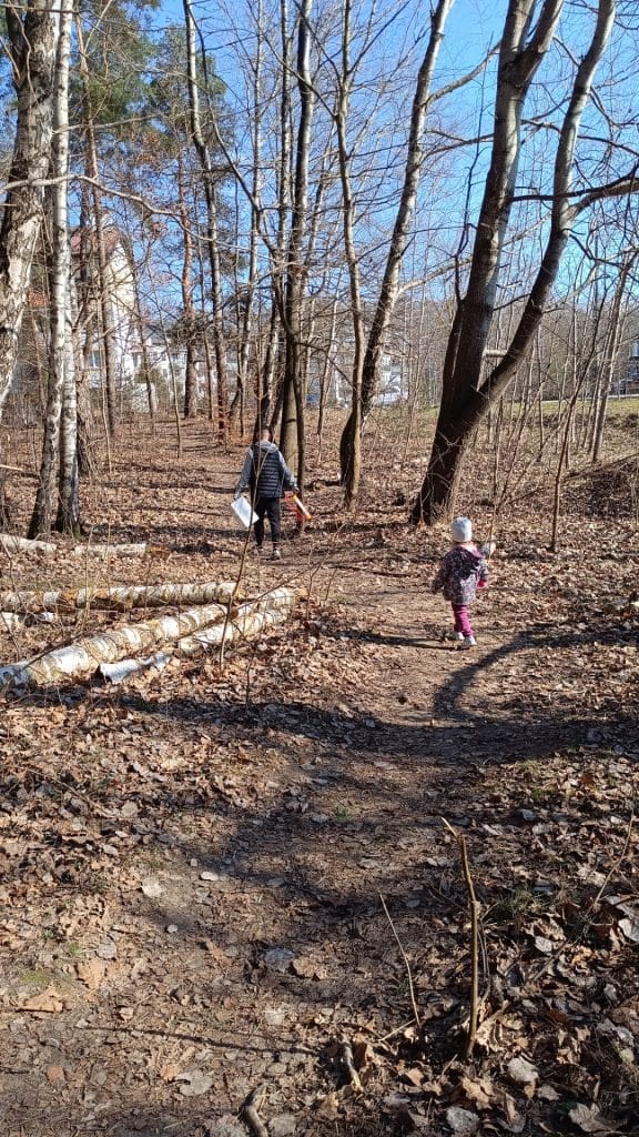 Grupa mieszkańc&oacute;w i dzieci sprzątających Lasek Pieczewski w słoneczny dzień, zbierających odpady.