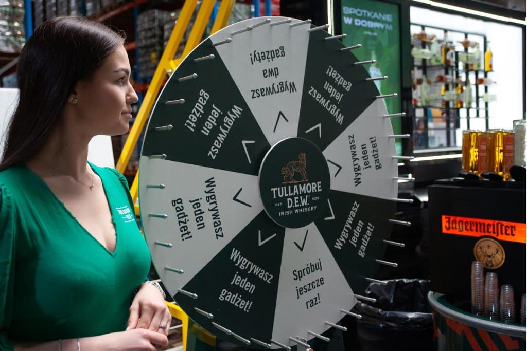 Kobieta przy kole fortuny na targach w Gdańsku, w tle stoiska z napojami i produkty branży HoReCa.