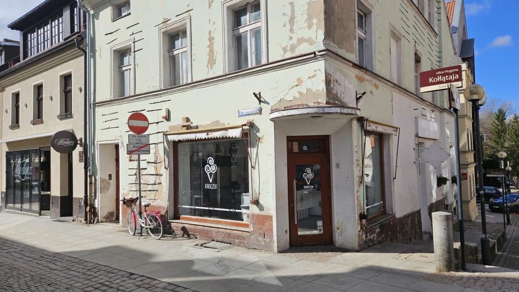 Stara kamienica na ulicy z widocznymi śladami remontu i zniszczeń na elewacji.