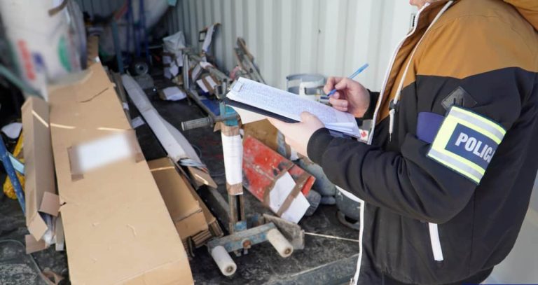 Policjant sporządza raport przy zniszczonym magazynie pełnym porozrzucanych przedmiot&oacute;w.